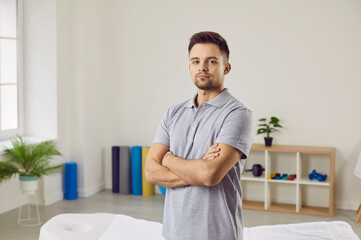Portrait of young male therapist or masseur in medical uniform posing in wellness studio or salon. Man physiotherapist or osteopath stand with arms crossed feel confident successful.