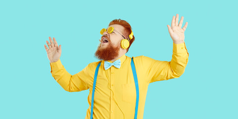 Funny happy fat bearded man in yellow shirt, turquoise blue bow tie, suspenders, headphones and...