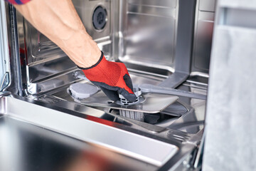 Concept maintenance service of home appliances. Worker cleans filter in the dishwasher. Male repairman checking food residue filters.