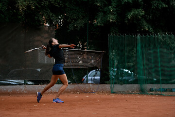 side view of active female tennis player with tennis racket in her hand behind her back