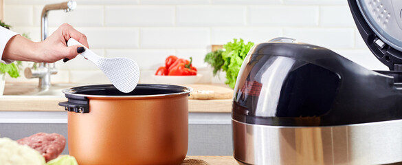 Female hand hold ladle over electric cooker in kitchen. Spoon with vegetables and modern multi...
