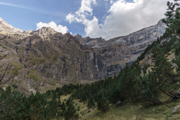 Cirque de Gavarnie with waterfall at massive high rock wall formation and forest in foreground in Pyrenees Mountains, Nouvelle-Aquitaine, France