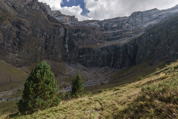 Cirque de Gavarnie with waterfall at massive high rock wall formation and fir tree on meadow in Pyrenees Mountains, Nouvelle-Aquitaine, France