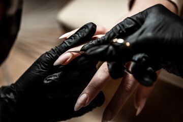 Manicurist is applying electric nail file drill to manicure on female fingers. Woman getting nail manicure. Beautician file nails to a customer. professional manicure tool