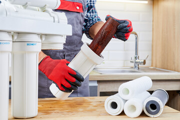 Plumber installs or change water filter. Replacement aqua filter. Repairman installing water filter cartridges in kitchen. Installation of reverse osmosis water purification system. - obrazy, fototapety, plakaty
