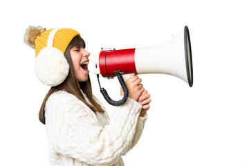 Little caucasian girl wearing winter muffs over isolated background shouting through a megaphone