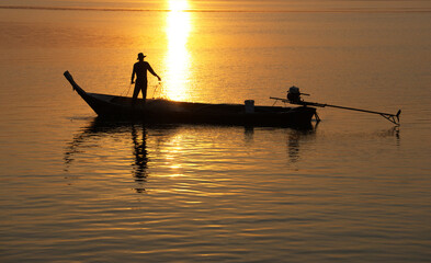 Silhouette of asian fisherman on a wooden boat preparing a net for catching freshwater fish in the early morning, Ban Sam Chong Tai, Ta Kua Thung, Phangnga, Thailand.