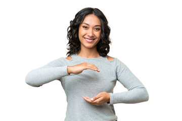 Young Argentinian woman over isolated background holding copyspace imaginary on the palm to insert...