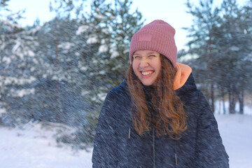 portrait of a beautiful cute girl in the park or forest, outdoors, woman having fun, laughing smiling at the nature. teenager in warm cloth. Blizzard and snow, snowflakes falling down