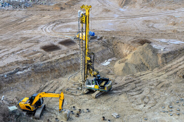 Drilling rig and excavator inside a pit at a construction site. Deep foundation machine for foundation works. Groung drilling for concrete placing into the borehole