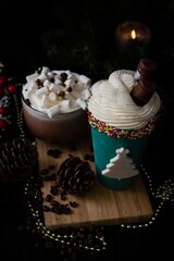 Glass shaped cake with whipped cream, marshmallows  and big mug of hot chocolate with marshmallows on black background. Winter holidays decoration.