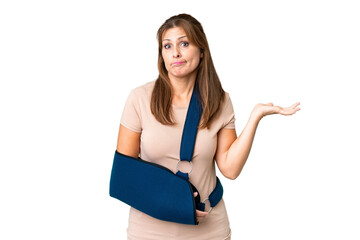 Fototapeta premium Middle age with broken arm and wearing a sling over isolated background having doubts while raising hands