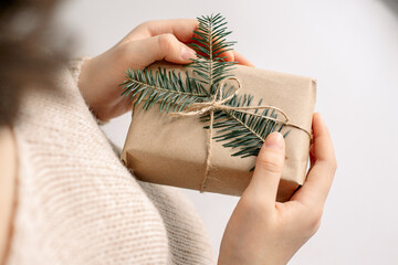 A woman is holding a box with a New Year's gift wrapped in kraft paper and decorated with a fir branch, a tourniquet. Top view, side view