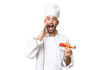 Young caucasian chef holding a sushi over isolated background with surprise and shocked facial expression