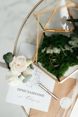 The concept of love and relationships. Wedding invitation. Gold rings in the moss with a gold casket on a marble table. Bouquet. Close-up.