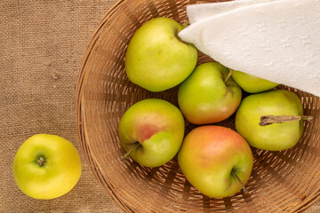 Several sweet green apples in a straw plate on a jute cloth, macro, top view.