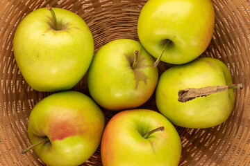 Several sweet green apples on a straw plate , macro, top view.