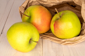 Naklejka na ściany i meble Three sweet green apples with a paper bag on a wooden table, macro.