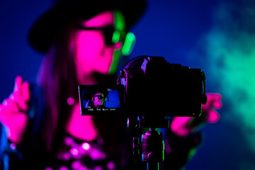 Backstage how operator working with professional camera. Videographer shoots music clip with actress or singer celebrity woman in dark studio with neon color light. - obrazy, fototapety, plakaty