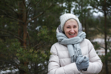 Portrait of happy beautiful elderly senior retired woman in age is playing, having fun with snow outdoors in forest or park at winter cold day, smiling, enjoy weather