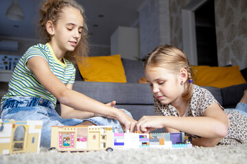 Two little girls sisters play with colorful toy blocks at home in the living room. Educational games for children. Mess in the playroom.