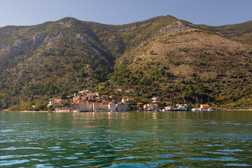  Red roof coastal town on the shore of Kotor bay. Montenegro mountains as background. Adriatic sea.