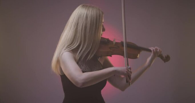 Beautiful blond woman playing violin against pink spotlight with smoke background.
