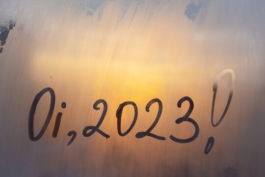 lettering Oi in Portuguese is hello in english and numbers 2023 paint with finger with streaks of water on splashed by foggy glass on orange sunset window