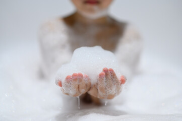 Close-up bubble foam on boy hands surrounded by soap suds when taking a bath in bathtub. Funny, healthcare lifestyle and hygiene concept.