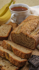 banana bread lies on a bright background surrounded by ingredients for cooking and a mug of tea. close up 