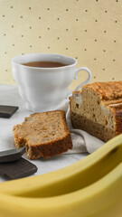 banana bread lies on a bright background surrounded by ingredients for cooking and a mug of tea. close up 