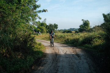 Obraz premium A young bearded cyclist is biking through a dirt path.