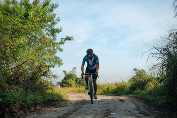 A young bearded cyclist is biking through a dirt path.