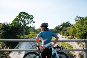 A young bearded cyclist on a bridge.