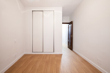 Empty room with a built-in wardrobe with white sliding doors and a dark wooden access door and plain white painted walls