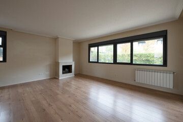 Empty room with black aluminum windows on one side, fireplace on the other and large white aluminum radiator