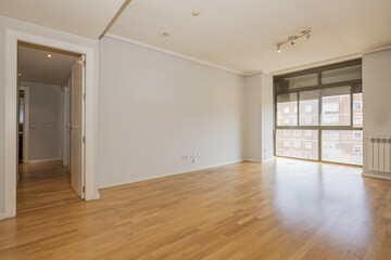 Empty room with gray walls, smooth white wooden interior doors, glass bay window with black aluminum and shutters, ceiling moldings and oak hardwood floors