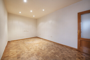 Empty room with plain white walls, interior wooden doors with display cabinets, built-in ceiling lights and oak hardwood floors