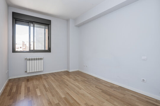 Empty room with blue walls, black anodized aluminum window, white aluminum radiator below and oak wood floors