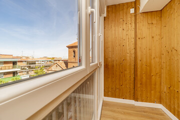 Closed terrace of a house with walls covered in wood, white aluminum windows and views of the city