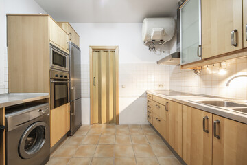 Kitchen with beech wood furniture, gray countertops and integrated stainless steel appliances