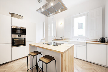Large kitchen with wooden furniture combined with white furniture without handles with a natural wood island with a hood and ceramic hob in the center