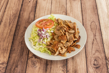 A typical kebab plate with grilled minced lamb meat on a skewer, a lot of lettuce, tomato and red onion salad on a wooden table