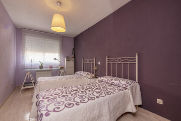 Bedroom with single beds with white metal headboards with patterned bedspreads in colors to match the walls and a study table under the window
