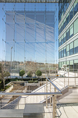 Front facade of an office building with lots of glass and metal, gardens with hedges and long pillars supporting the roof