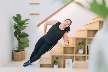 overweight woman using stairs workout indoors living room side plank. motivated fat woman side plank on stairs workout using healthy concept. chubby woman side balance plank stairs burn calories fat