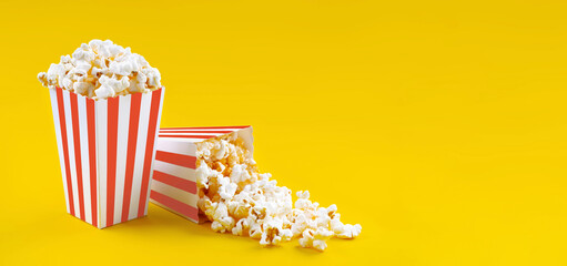 Two red white striped carton buckets with tasty cheese popcorn, isolated on yellow background. Box...