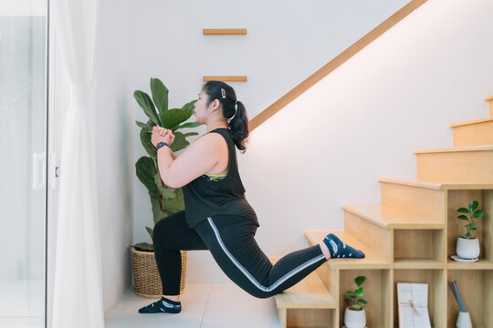 Fat Exerciser Workout Using Stairs Indoors Living Room Single Leg Lunge. Overweight Determined Woman Lunge Stairs For Exercising Legs. Motivated Chubby Woman Trying Single Leg Lunge Pose On Stairs