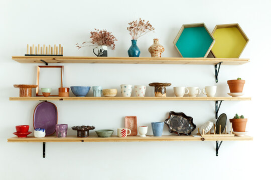 Handmade ceramic crockery and craft pottery jug, jars and cups standing on shelves in creative studio or potter store. Different handicraft clay earthenware bowls in artisan craftsman classes workshop