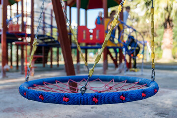 Large mesh swing in the playground. Round swing seat made of mesh in playground. Empty blue and red rope web nest for swinging closeup.
